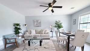 Uma sala de estar moderna com sofá, mesa de centro, mesa de jantar, cadeiras e ventilador de teto.