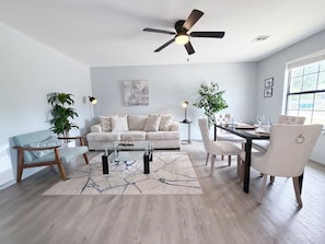 Una sala de estar moderna con sofá, mesa de centro, mesa de comedor, sillas y un ventilador de techo.