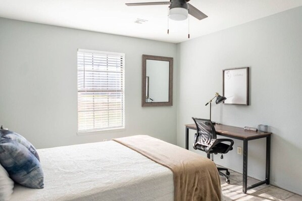 A bedroom with a bed, a desk, a chair, a ceiling fan, and a window with blinds.