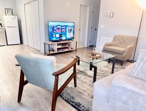 Una sala de estar con televisor, sofá, sillón y una mesa de centro.
