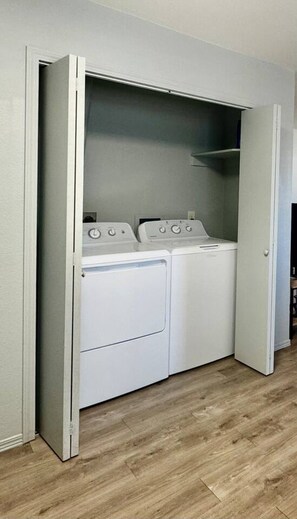 A laundry room with a built-in washer and dryer, wooden flooring, and a door leading to another room.