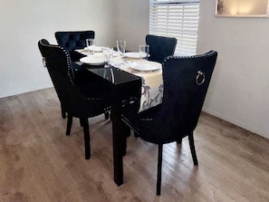 Un comedor con una mesa rectangular, cuatro sillas y una ventana con persianas.