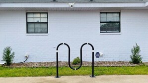 A white building with two windows, a black metal structure in front, and a small sign on the right.