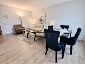 Een moderne woonkamer met een bank, fauteuils, een salontafel en een eettafel voor vier personen.