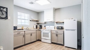 A modern kitchen with light wood flooring, beige cabinets, a white stove, and a white refrigerator.