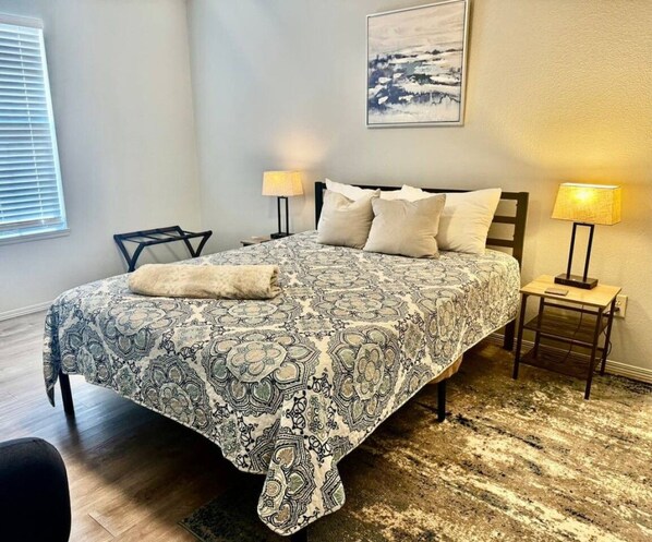 A bedroom with a patterned bedspread, two bedside lamps, a headboard, and a framed picture on the wall.