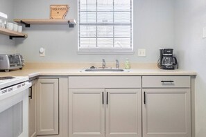 A kitchen with a white countertop, a sink, a toaster, a coffee maker, and cabinets.