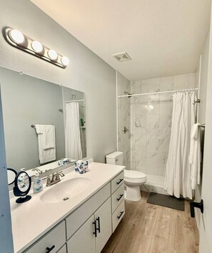 A modern bathroom with a white vanity, a toilet, a shower with a glass door, and a mirror with lights above.