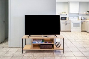 A modern kitchen with a flat-screen TV on a wooden stand, a microwave, a toaster, and cabinets.
