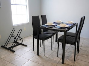 A dining area with a table set for four, four black chairs, and a black metal stand.