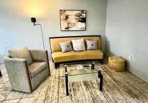 A living room with a sofa, armchair, glass coffee table, and a rug.