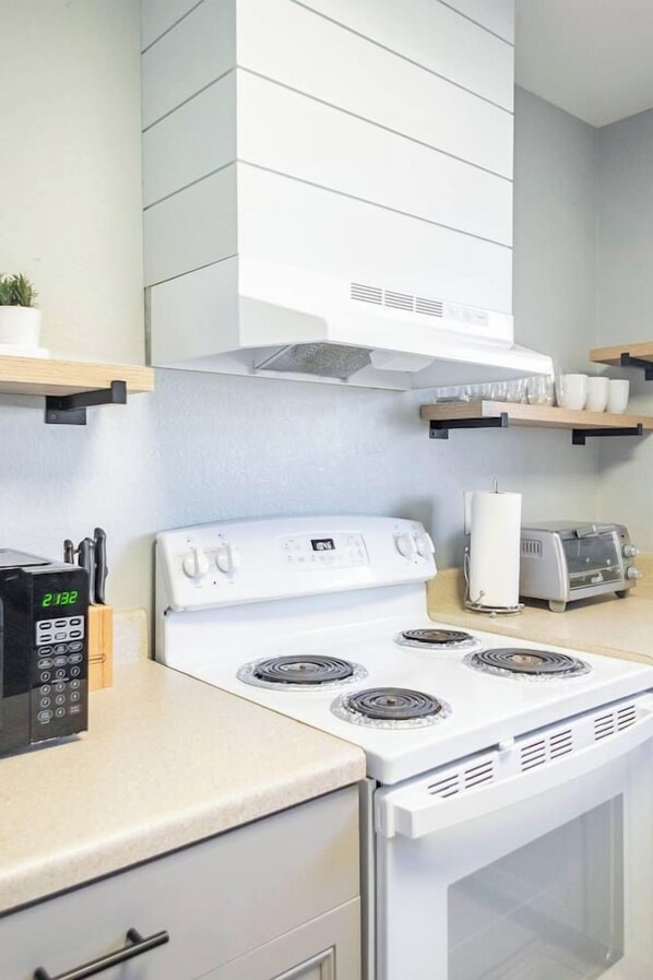 A kitchen with a white stove, a toaster, and a microwave. There are wooden shelves above the stove.