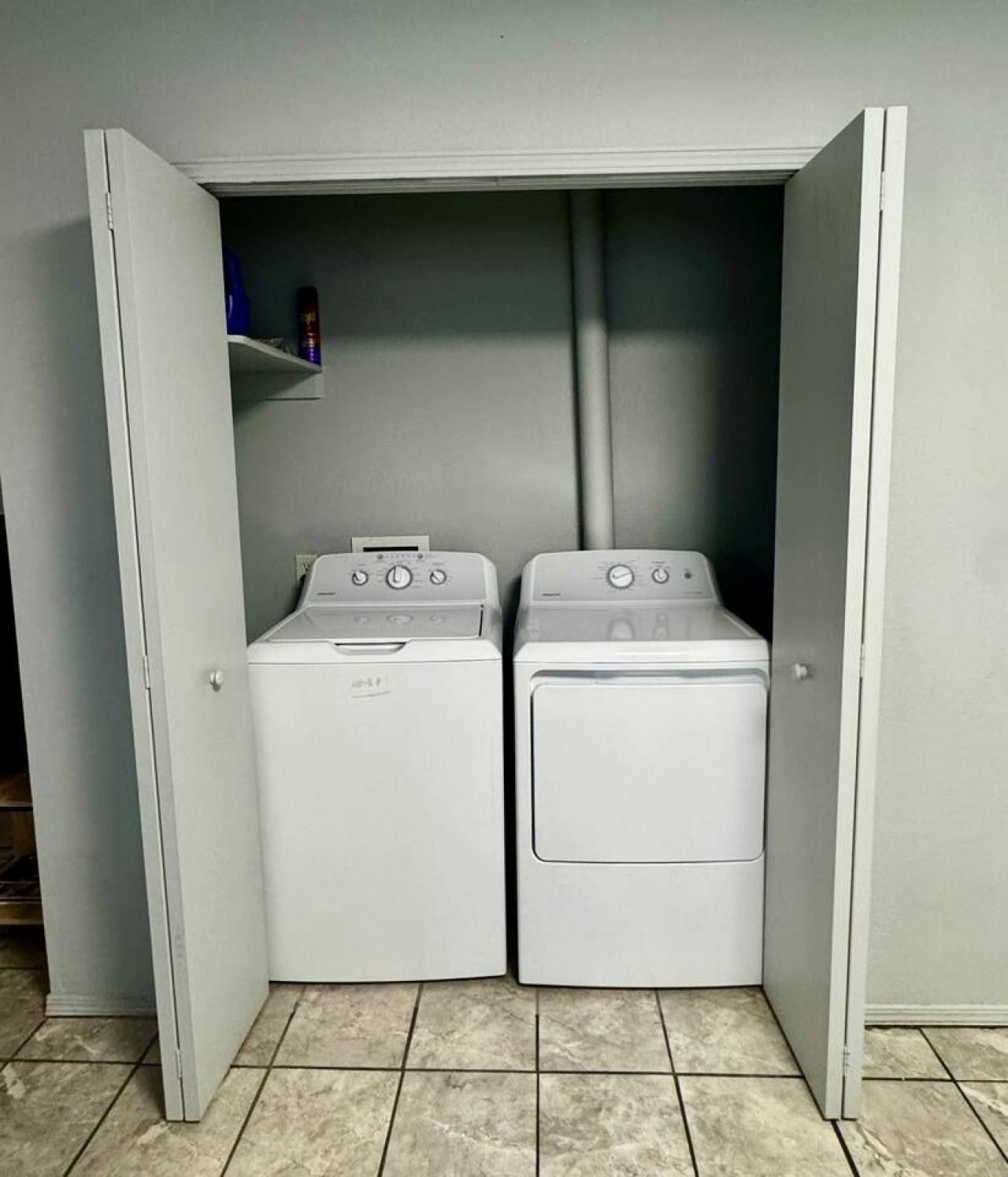 A laundry room with two front-loading washing machines and a shelf with items.