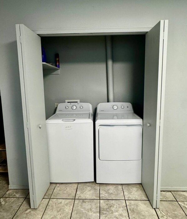 A laundry room with two front-loading washing machines and a shelf with items.