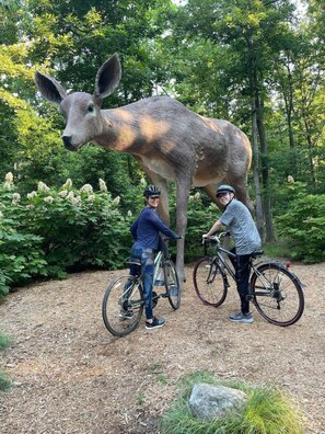 Two people on bicycles near a large deer statue in a wooded area.