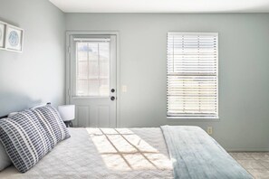 A bedroom with a bed, a door, and a window with blinds.