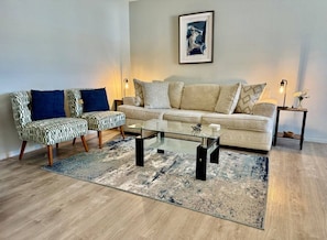 A living room with a sofa, two armchairs, a glass coffee table, and a patterned rug.