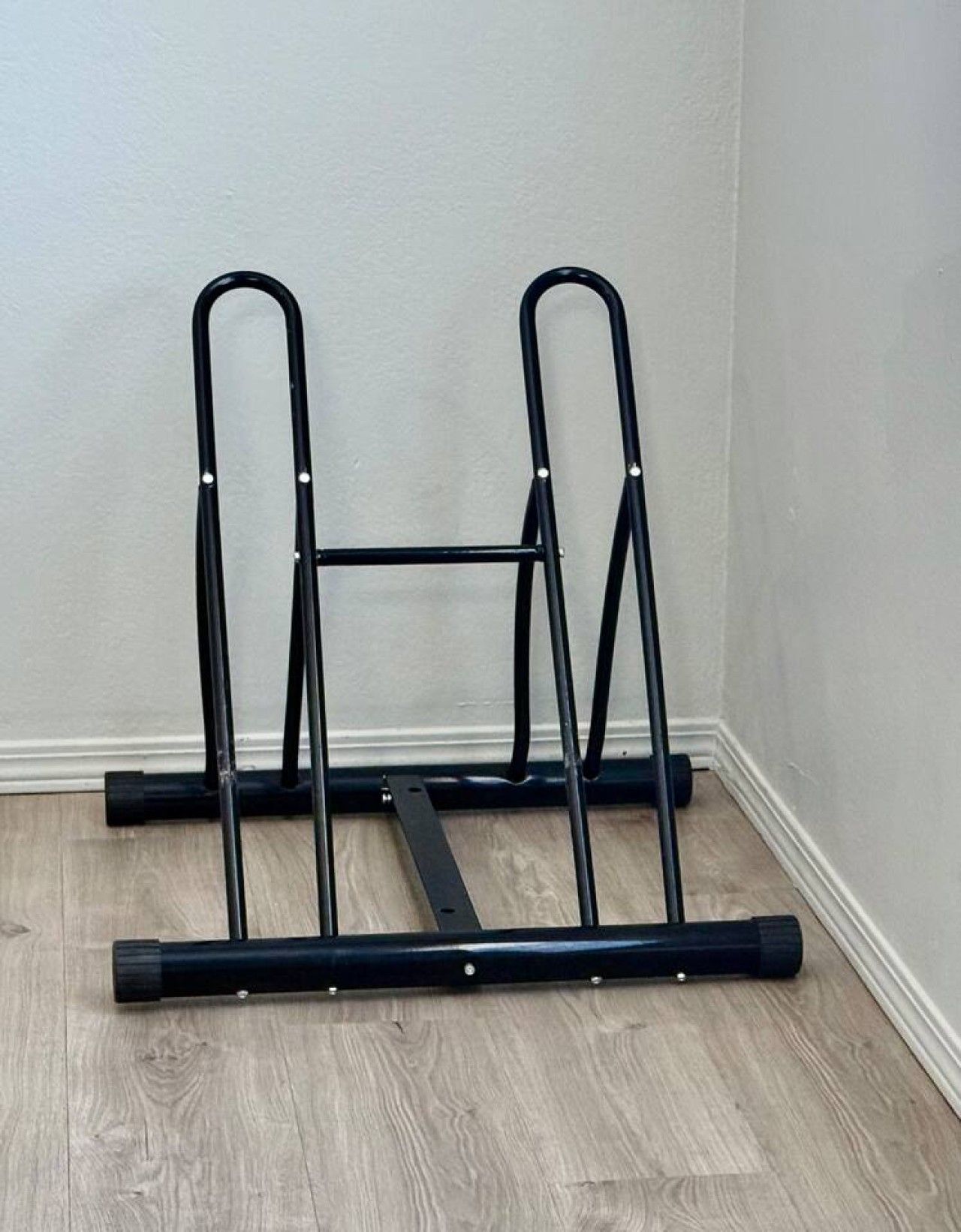 A corner with a black metal rack against a white wall and wooden flooring.