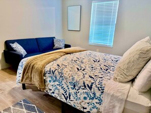 Un dormitorio con cama, sofá azul y ventana con persianas.