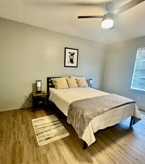 A bedroom with a bed, a nightstand, a ceiling fan, and a window with blinds.