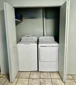 A laundry room with two white front-loading washing machines and a shelf above them.