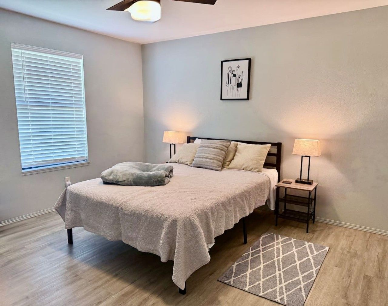 A bedroom with a bed, bedside lamps, a rug, and a wall-mounted picture.
