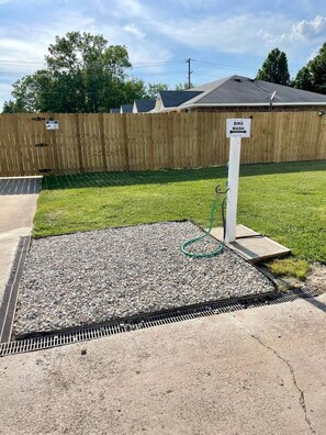 A gravel area with a hose, a wooden fence, and a house in the background.