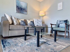 A living room with a glass coffee table, a sofa, a chair, and a lamp.