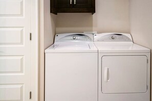 A laundry room with two stacked washers and dryers, a white door, and a dark wooden cabinet above.