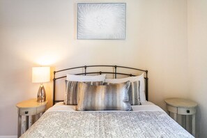 Ein Bett mit einem gemusterten Überwurf, einem Metall-Kopfteil und zwei Nachttischen mit Lampen.