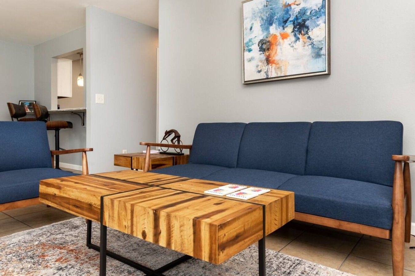 Un salon moderne avec un canapé bleu, une table basse en bois et une œuvre d’art abstraite accrochée au mur.