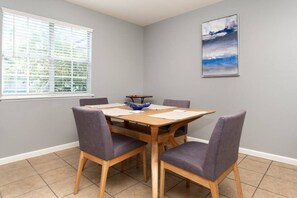 Uma área de refeições com uma mesa de madeira, quatro cadeiras e uma janela com persianas.