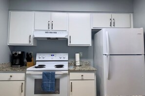 A kitchen with white cabinets, a stove, a refrigerator, and a coffee maker.