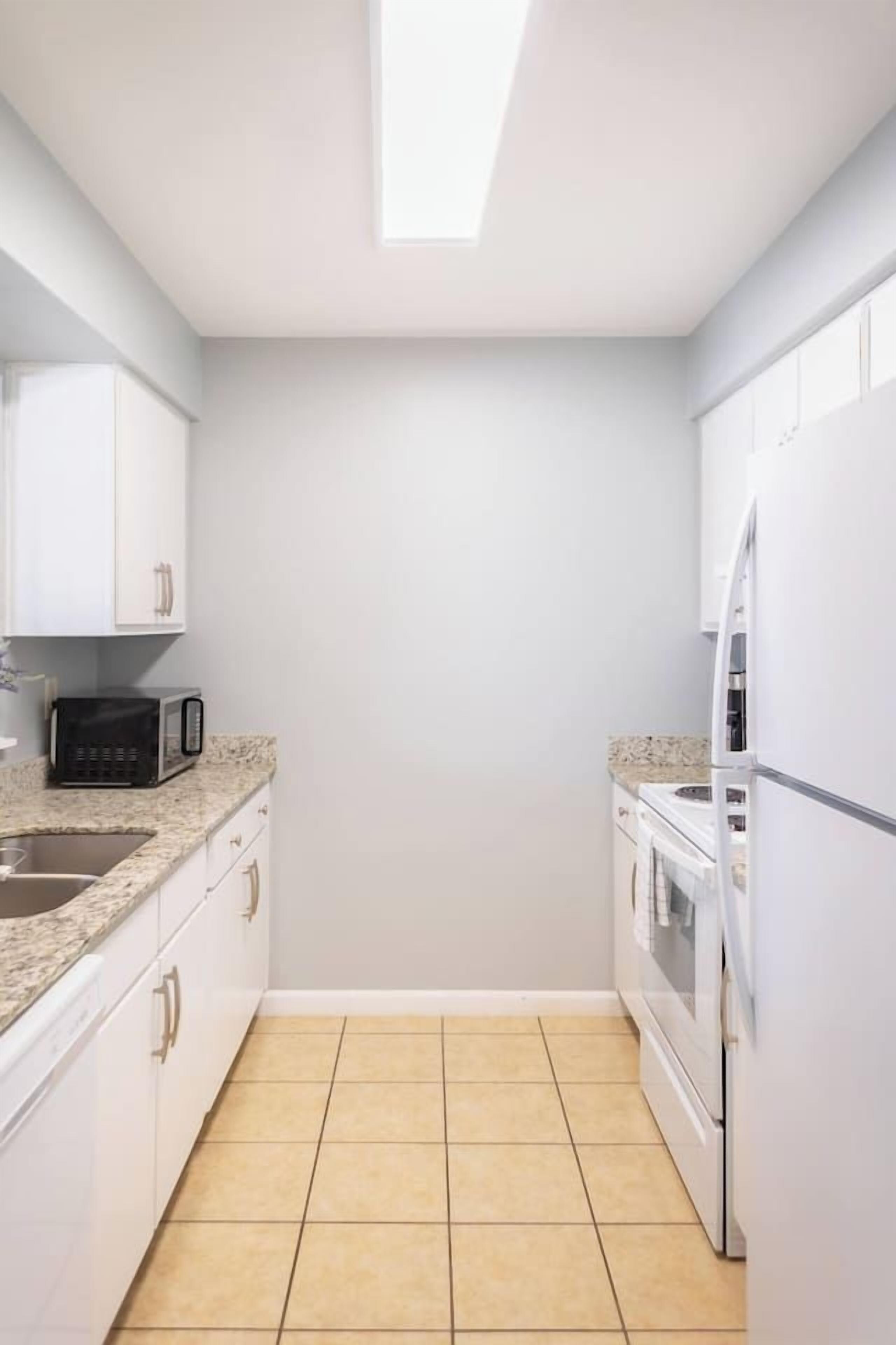 Una cocina compacta con gabinetes blancos, un microondas y un refrigerador.