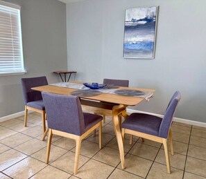 A dining area with a wooden table and four chairs, a blue decorative bowl, and a framed abstract painting on the wall.