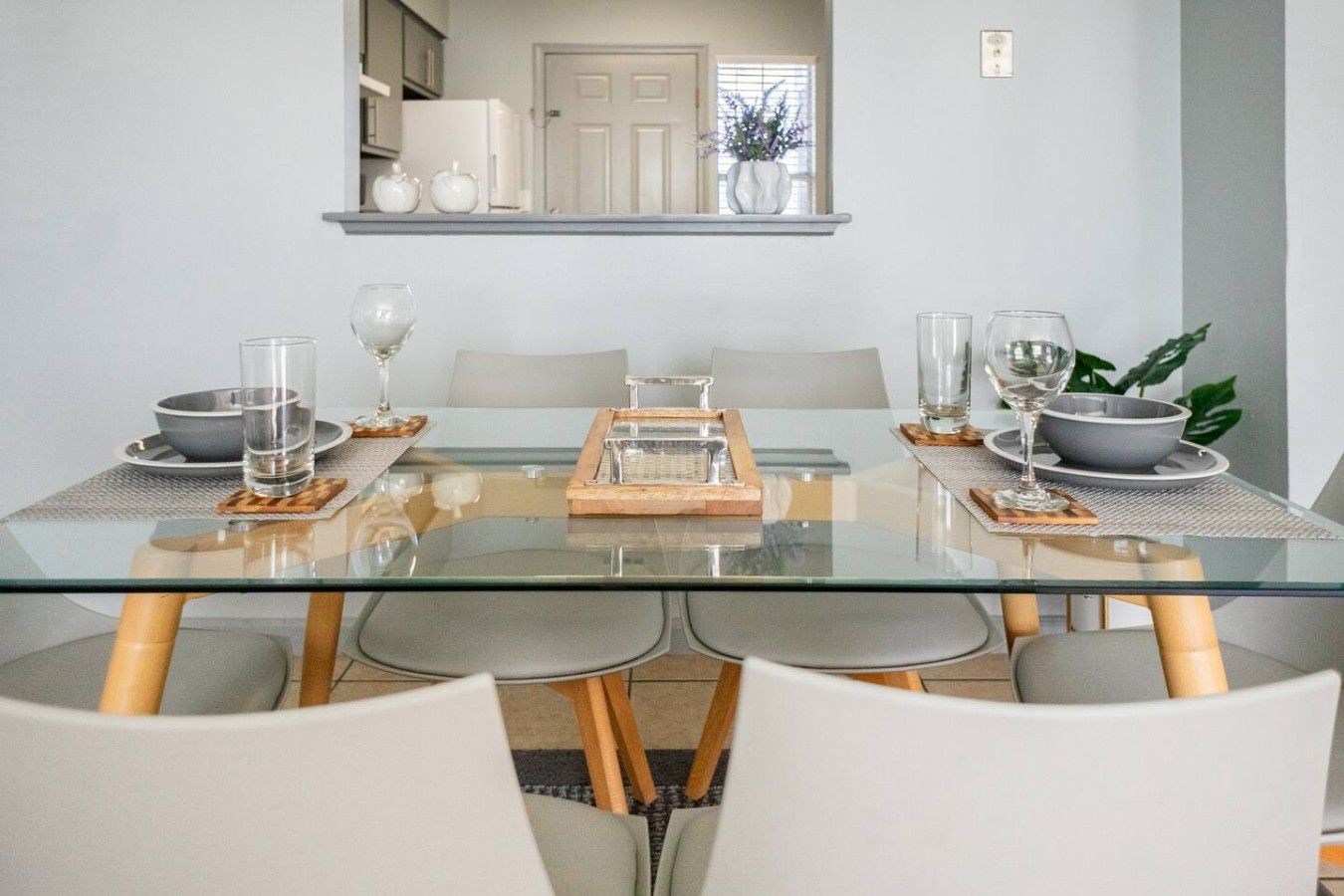 Un espace repas moderne avec une table en verre, des chaises blanches et un grand plateau de service placé au centre.