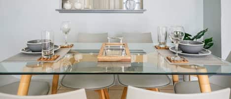 Un espace repas moderne avec une table en verre, des chaises blanches et un grand plateau de service placé au centre.