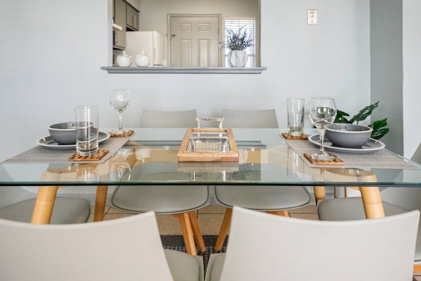 Uma sala de jantar moderna com mesa de vidro, cadeiras brancas e um suporte central para servir.