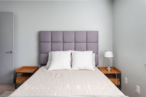Une chambre à coucher avec un lit, deux tables de chevet, une lampe et une porte.