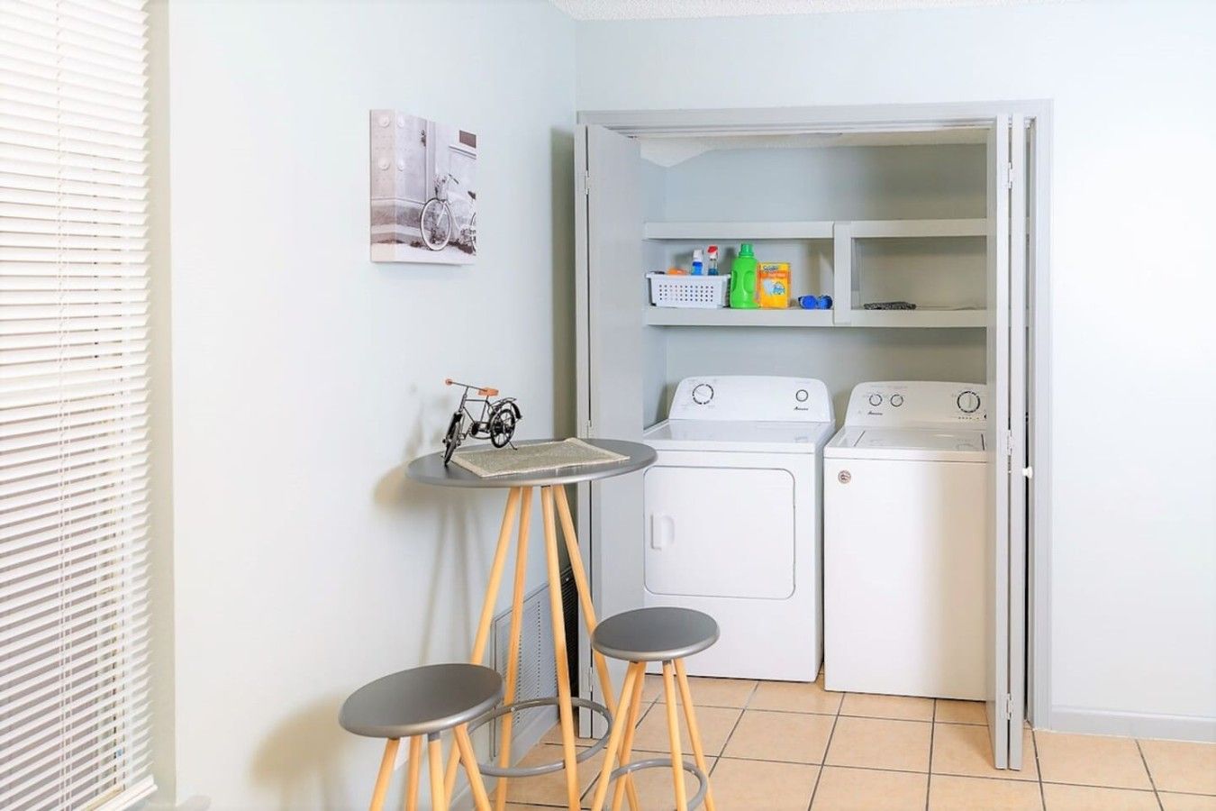 Un espace buanderie compact comprenant un lave-linge, un sèche-linge et une petite table avec des tabourets.