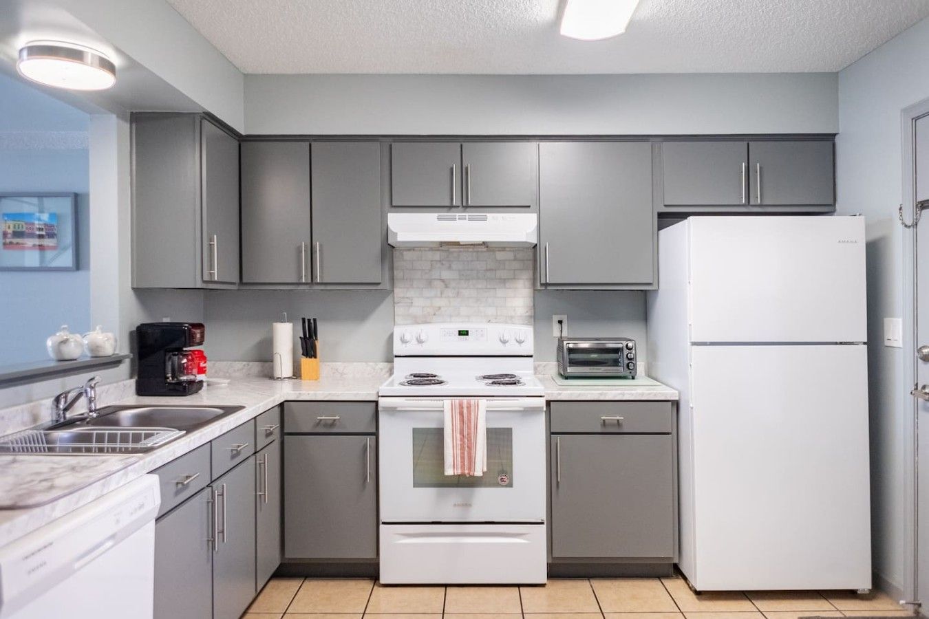 A compact kitchen with grey cabinets, a white stove, a toaster, and a refrigerator.