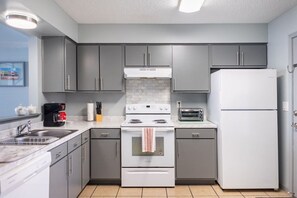 A compact kitchen with grey cabinets, a white stove, a toaster, and a refrigerator.