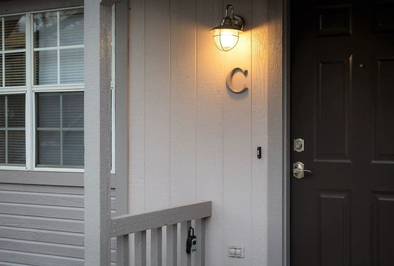 A house exterior with a white door, a black doorbell, and a light fixture above the door.