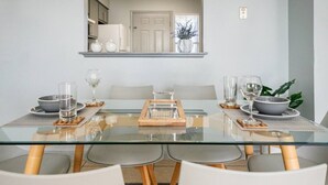 A modern dining area with a glass table, white chairs, and a central serving tray.