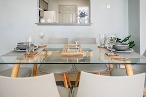 A modern dining area with a glass table, white chairs, and a central serving tray.