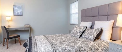 A bedroom with a bed, a desk, a chair, and a window.