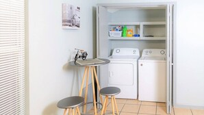 A compact laundry area with a washing machine, dryer, and a small table with stools.