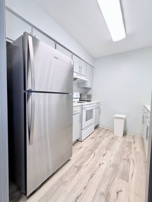 Uma cozinha moderna com eletrodomésticos de aço inoxidável, armários brancos e piso de madeira clara.