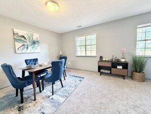 A dining area with a table and chairs, a rug, a bookshelf, and a window.