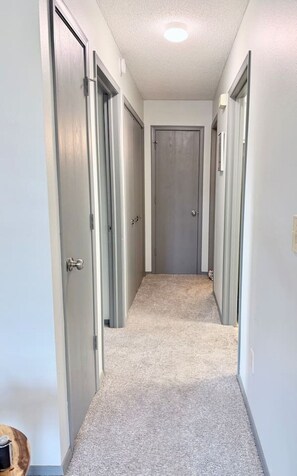 Un pasillo estrecho con piso alfombrado y puertas a ambos lados que dan a habitaciones.